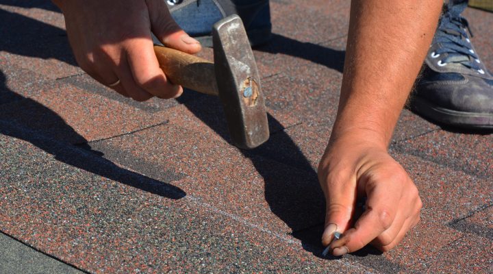 Roofing contractor laying asphalt shingles. House roofing construction with roofing shingles. Roofer hammering a nail in asphalt shingles on the house roof.
